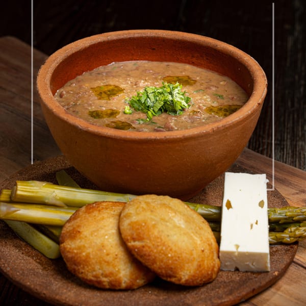 Hearty bean stew in a rustic bowl, served with flatbread, pickled vegetables, and feta cheese.