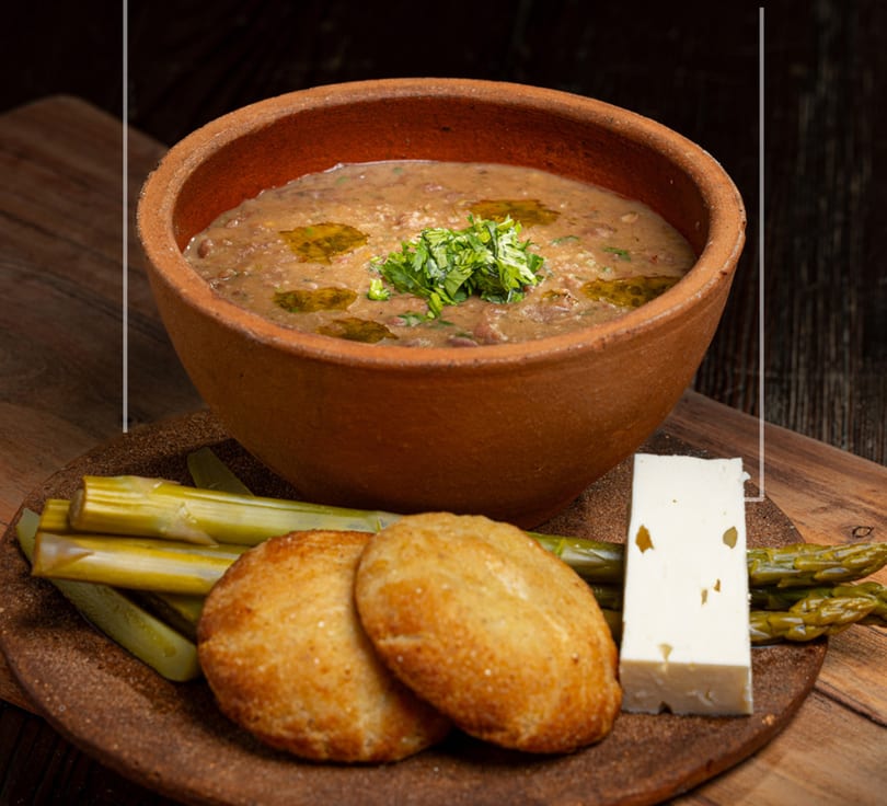 Hearty bean stew in a rustic bowl, served with flatbread, pickled vegetables, and feta cheese.