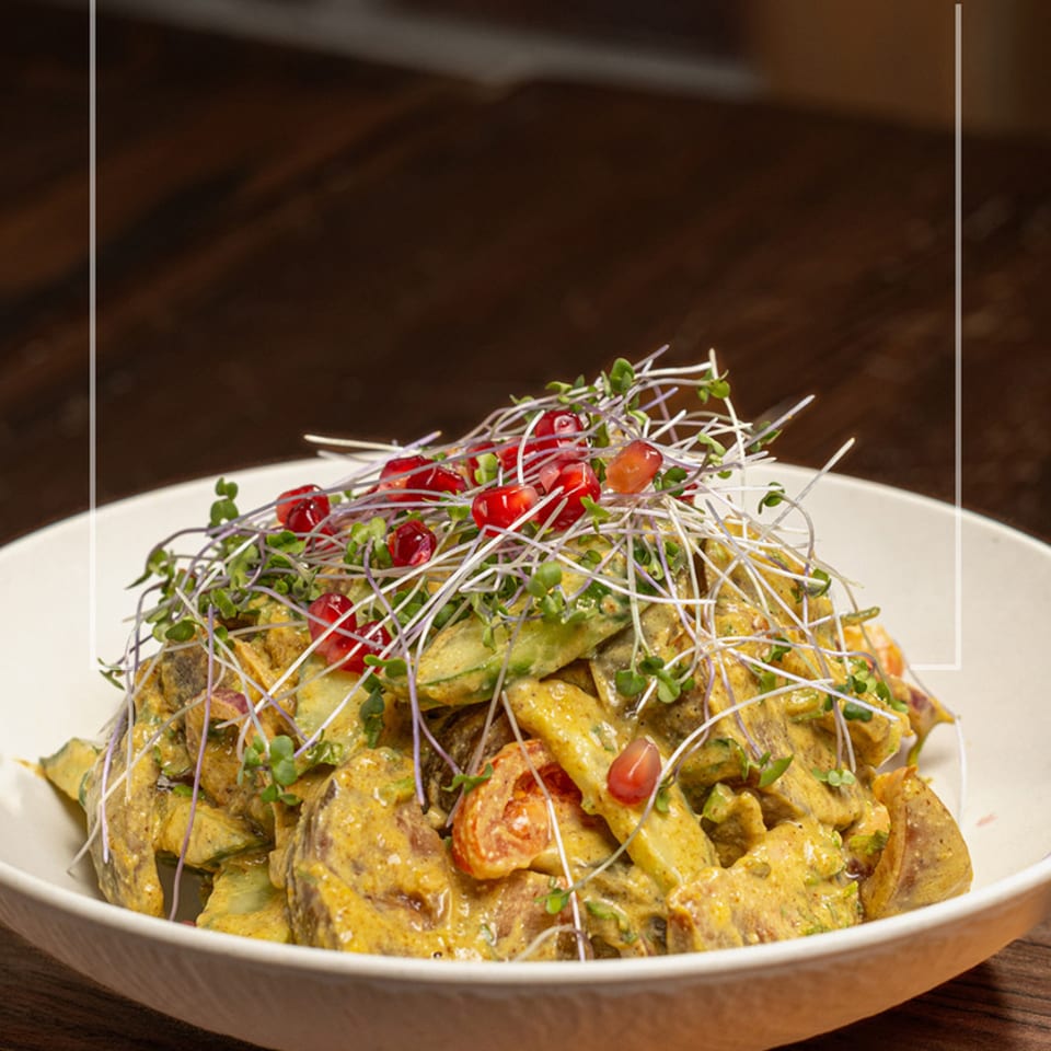 A vibrant salad with yellow dressing, topped with microgreens and pomegranate seeds in a white bowl.