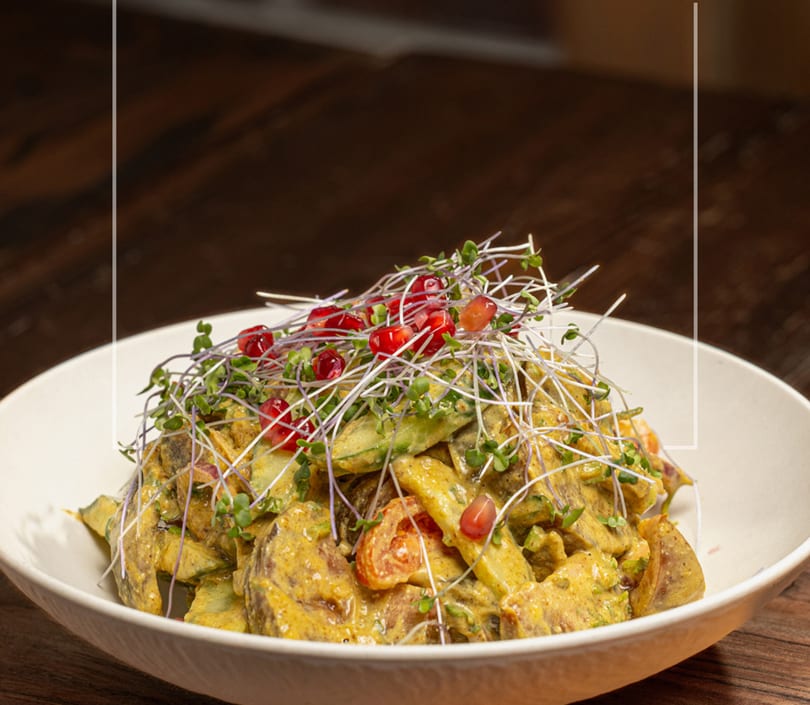 A vibrant salad with yellow dressing, topped with microgreens and pomegranate seeds in a white bowl.