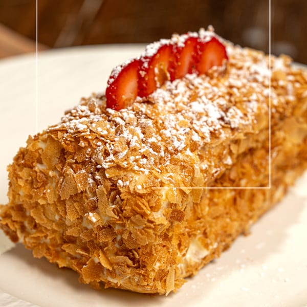 Mille-feuille pastry topped with powdered sugar and sliced strawberries on a white plate.