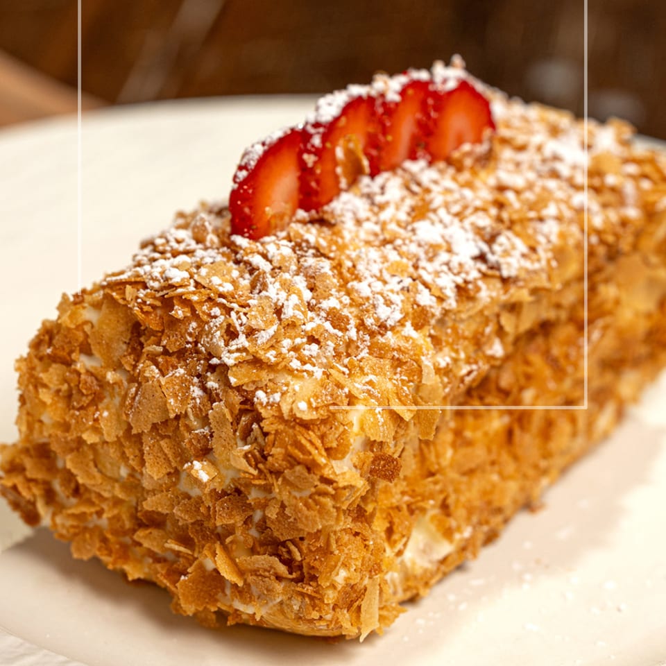 Mille-feuille pastry topped with powdered sugar and sliced strawberries on a white plate.