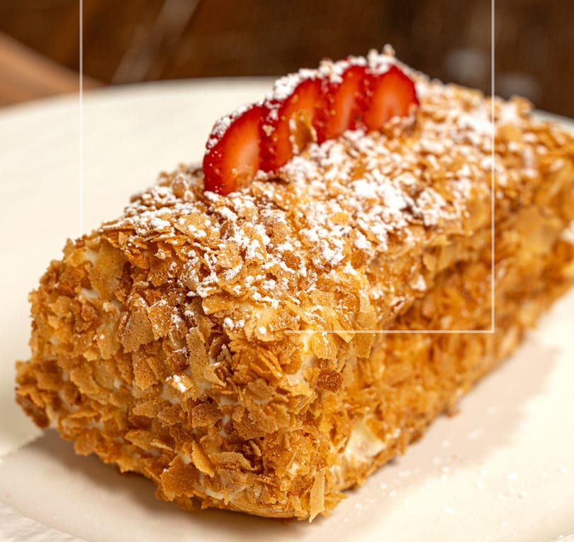 Mille-feuille pastry topped with powdered sugar and sliced strawberries on a white plate.